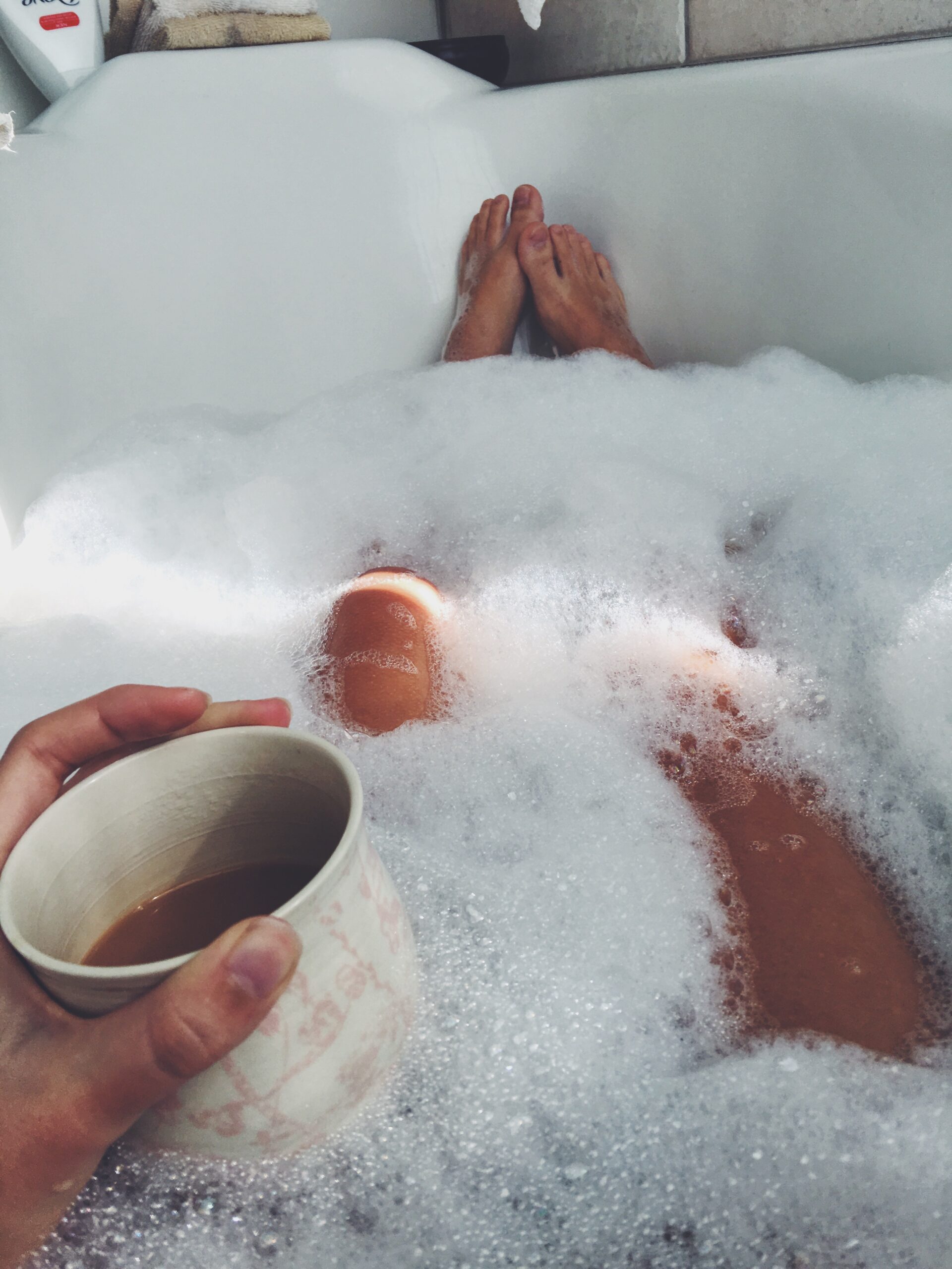 girl in sudsy bathtub with coffee in hand