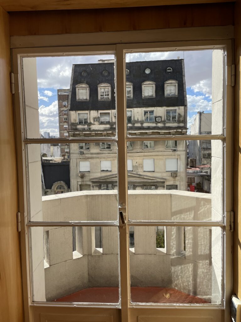 A window opens out to an office building on the other side of palacio barolo